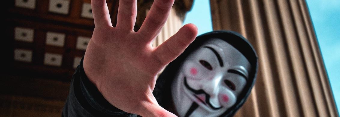 Hacker in a Guy Fawkes mask reaching toward the camera